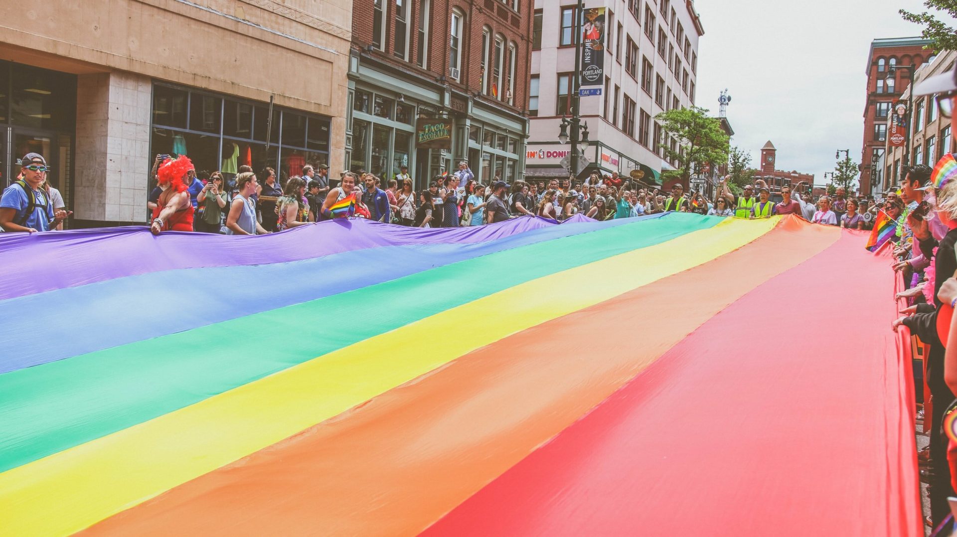 Portland, Maine residents carry the large rainbow flag down Congress Street during the annual Pride parade (Photo by Mercedes Mehling | Unsplash)